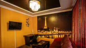 Un salon moderne avec un canapé, un téléviseur, une petite table et une vue sur la Tour Eiffel la nuit.
