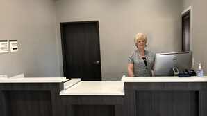 Zona de recepción con un escritorio de madera oscura, una computadora y una puerta al fondo.