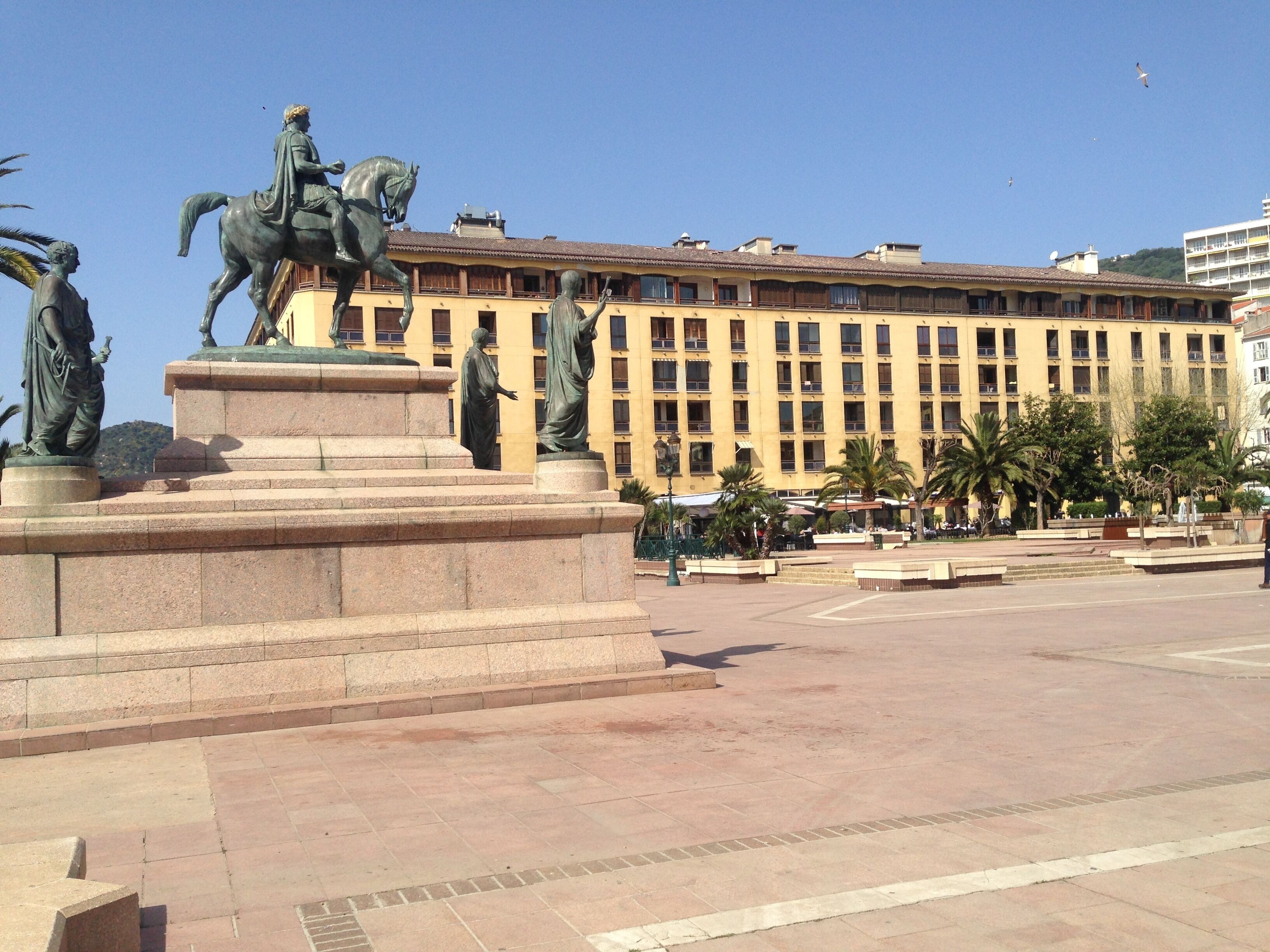 Une place publique ornée d’une statue représentant un homme à cheval et d’une autre statue représentant une femme.