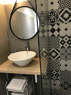 A bathroom with a round mirror, a white sink, and patterned tiles. - Loft for 2–4 people, Place du Diamant, downtown, with garage. (Ajaccio)