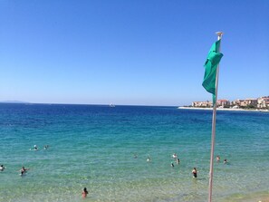 A beach with clear turquoise water, a flagpole with a green flag, and a distant boat. - Loft for 2–4 people, Place du Diamant, downtown, with garage. (Ajaccio)