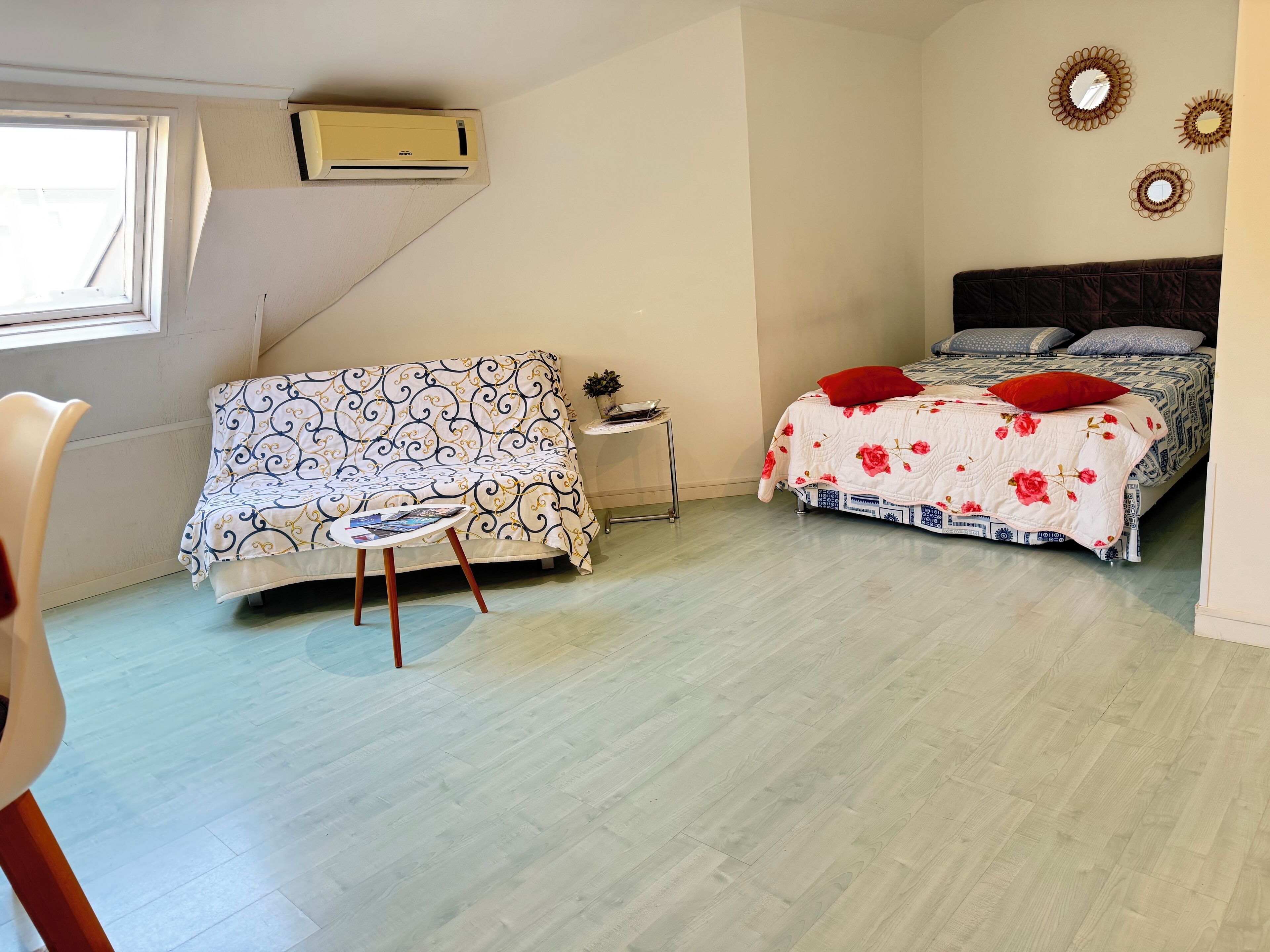 A bedroom with a bed, a sofa, a small table, and a window.