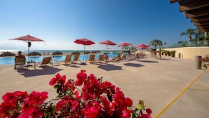 A poolside area with lounge chairs and red umbrellas, overlooking a clear blue sky and ocean. - New Oceanfront Condo Grand Venetian (Puerto Vallarta)