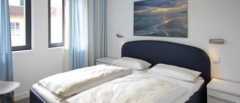Un dormitorio con dos camas, una mesita de noche, una silla y una ventana con cortinas.