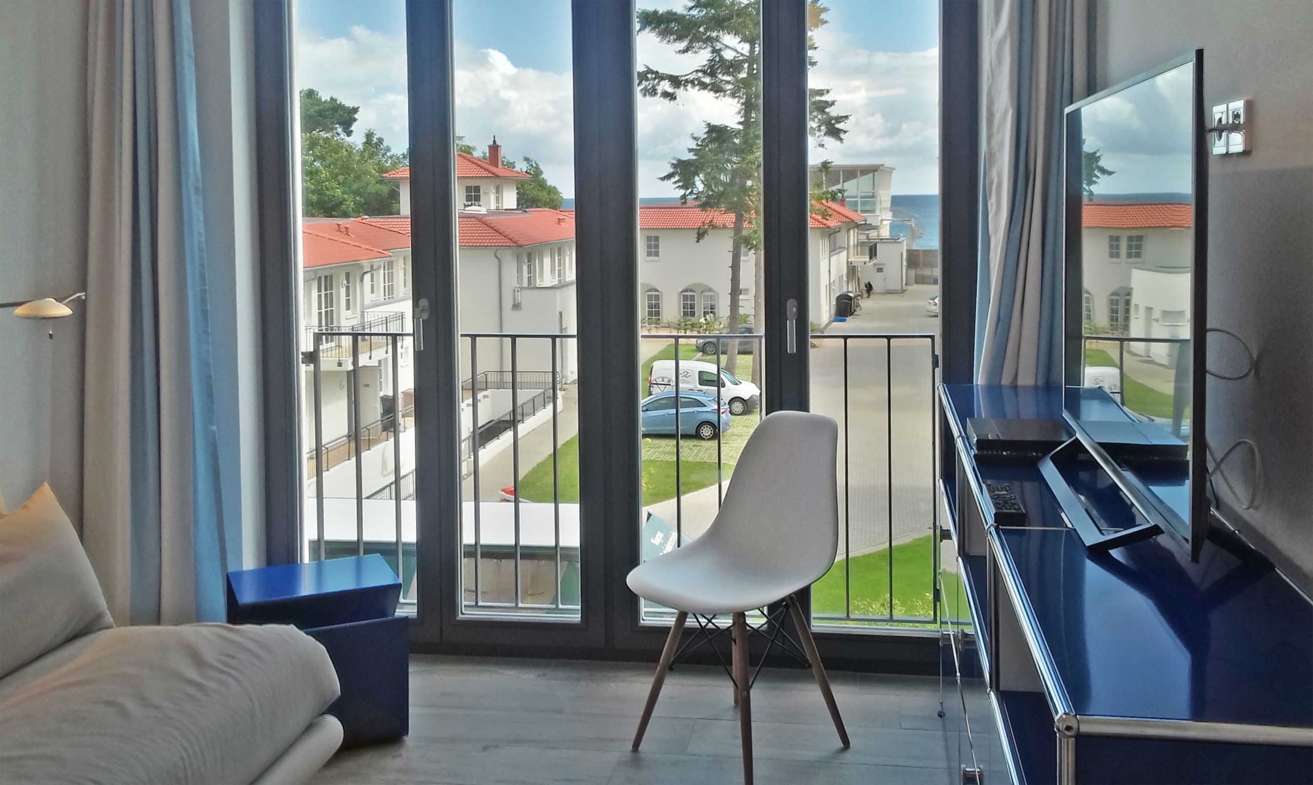 A balcony with a view of a residential street, a white chair, and a TV stand.