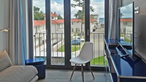 Un balcon donnant sur une rue résidentielle, une chaise blanche et un meuble pour la télévision.