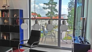 Une pièce moderne avec une grande fenêtre, une bibliothèque, une chaise noire et une petite table.