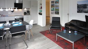 Un salon moderne avec un canapé en cuir noir, une table basse et un coin repas avec une table dressée pour quatre personnes.