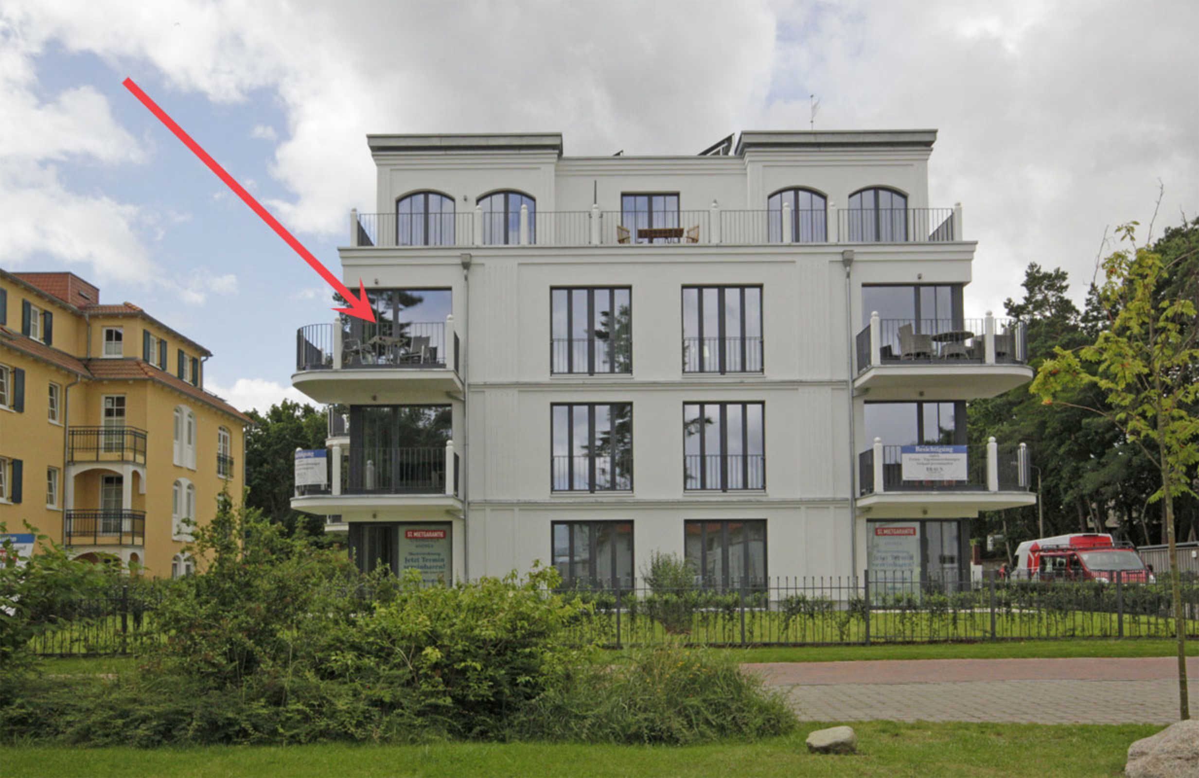 A multi-story building with balconies, a sign indicating a restaurant, and a red arrow pointing to a specific area.