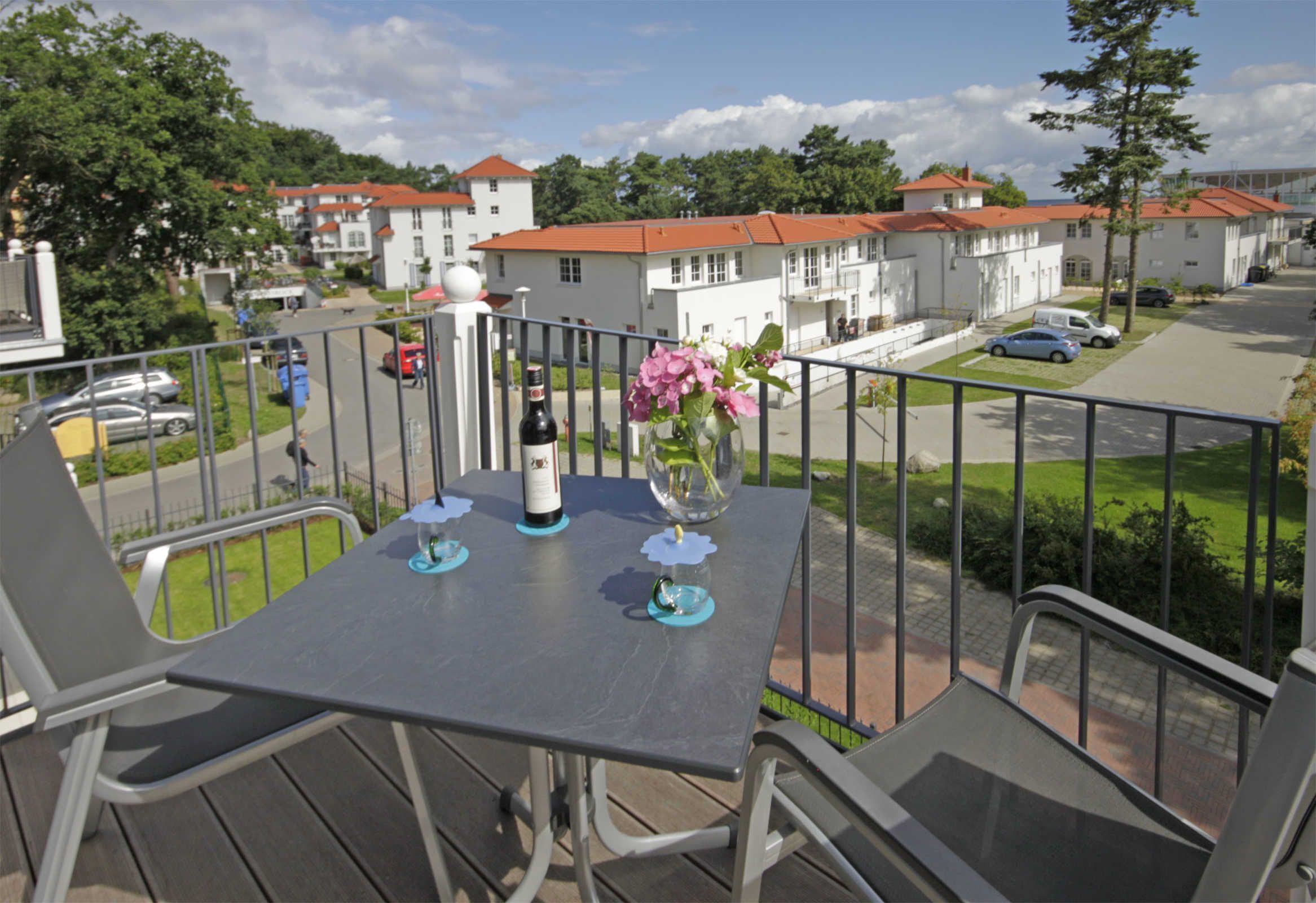 Un balcon avec une table dressée pour deux personnes, une bouteille de vin et un vase rempli de fleurs.