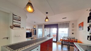 Eine moderne Küche mit einer zentralen Kochinsel, Pendelleuchten und einem Essbereich mit Tisch und Stühlen.