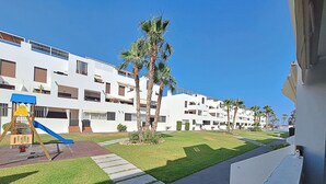 Ein Wohngebäude mit Spielplatz, Palmen und blauem Himmel.
