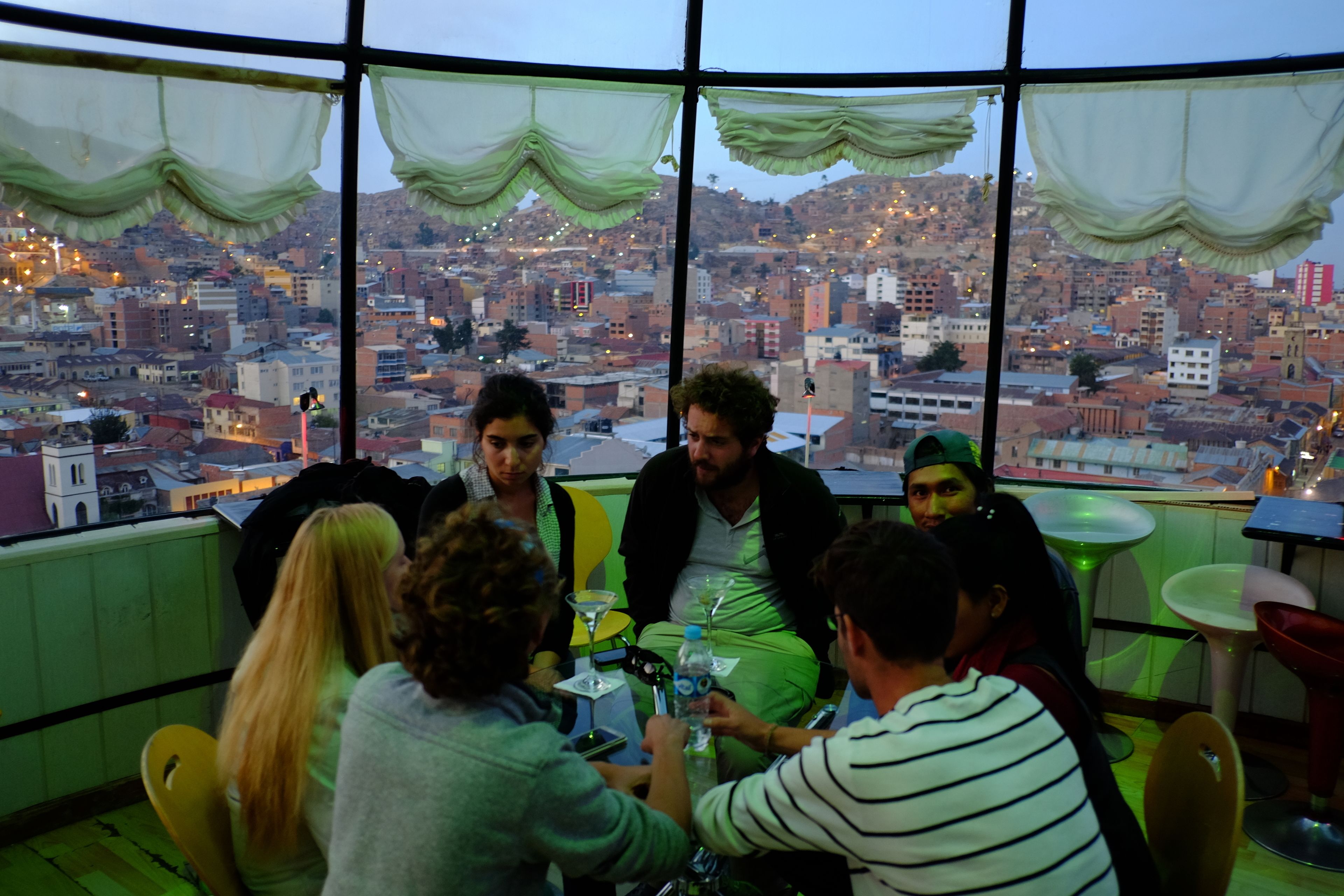 Um grupo de pessoas sentadas à volta de uma mesa dentro de um espaço com grandes janelas com vista para a paisagem urbana.