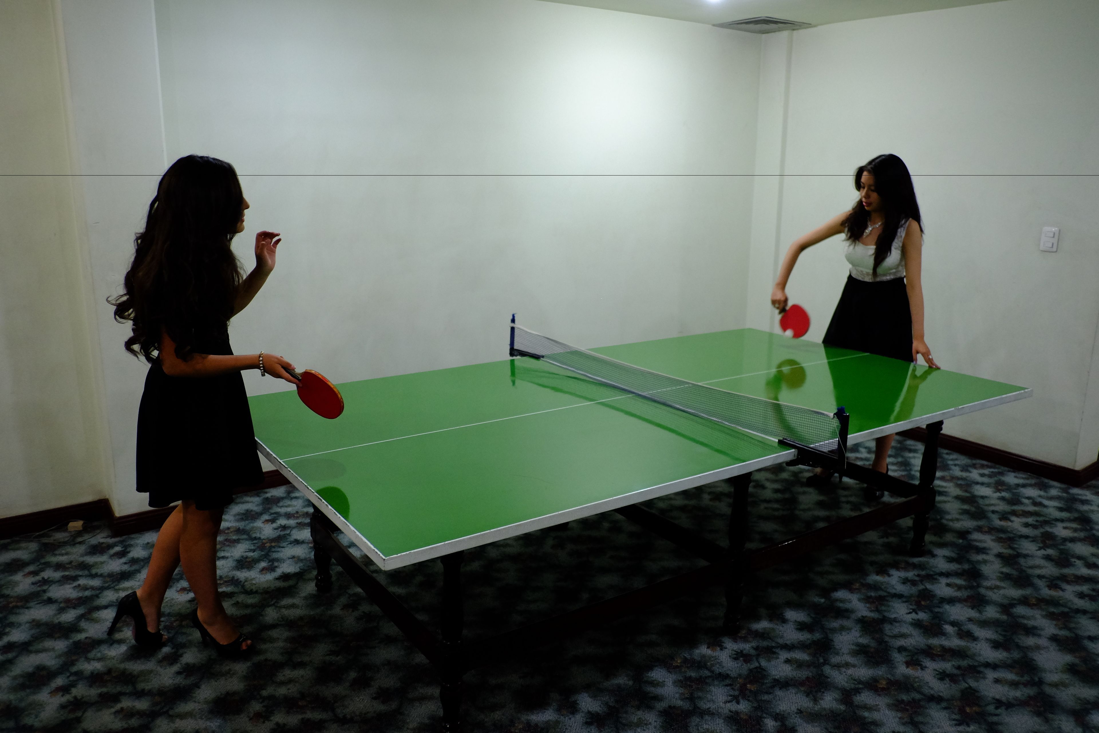 Två personer spelar bordtennis i ett rum med ett grönt bord och ett mönstrat golv.