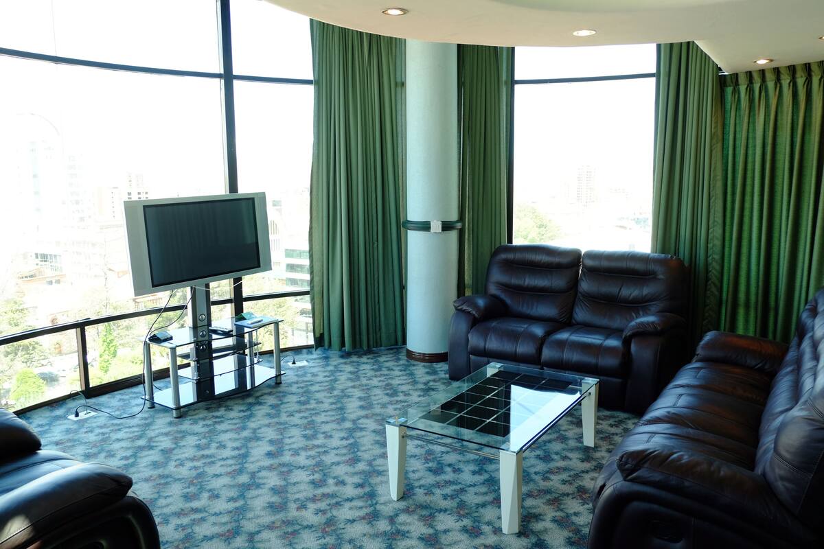 Ein Wohnzimmer mit großem Fenster, einer Ledersofa, einem Glastisch und einem Flachbildfernseher.