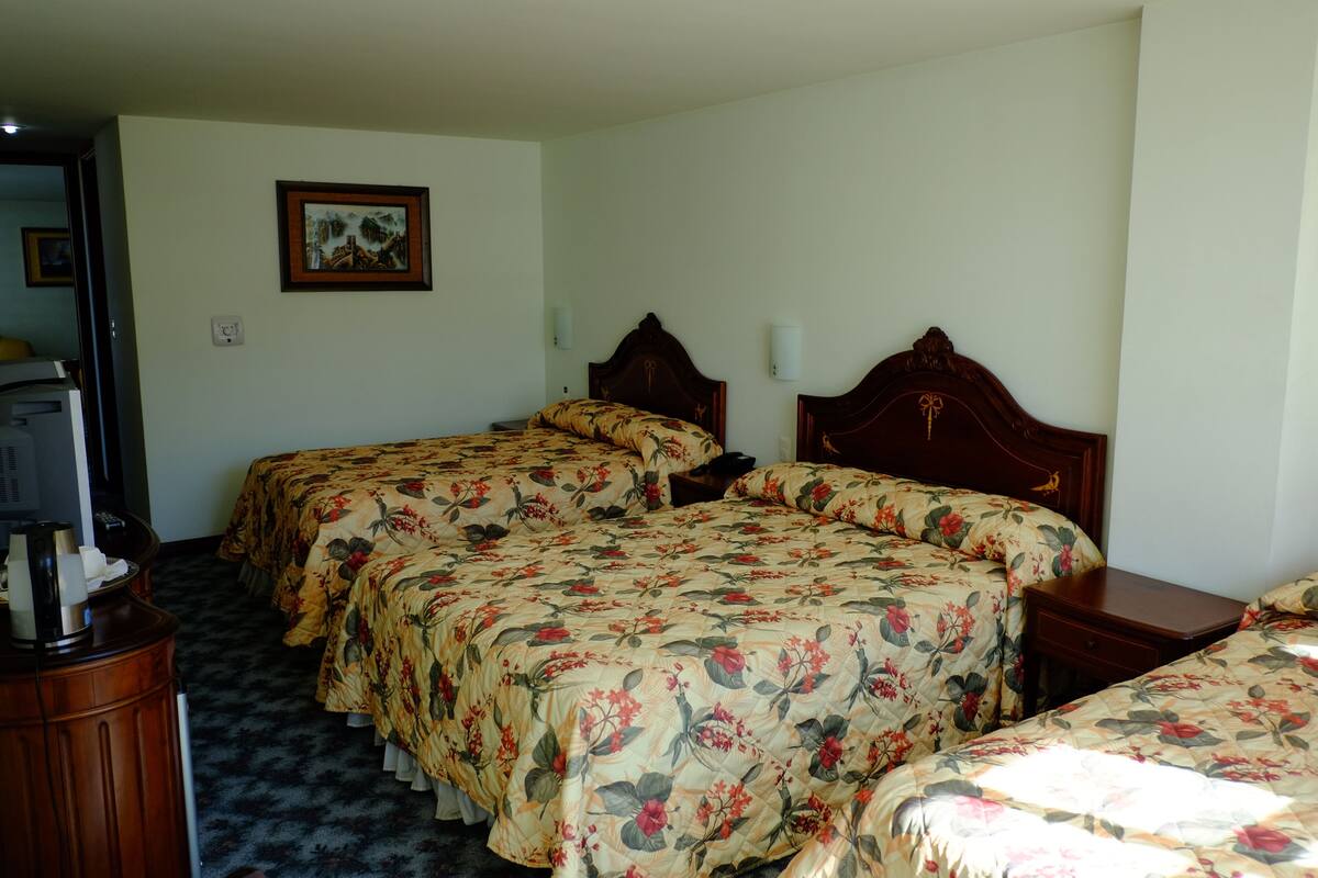 Ein Hotelzimmer mit zwei Betten, einem Holzkopfteil, einem gerahmten Bild an der Wand und einem kleinen Tisch mit einer Lampe.