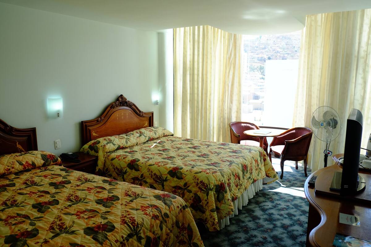 Ein Hotelzimmer mit zwei Betten, einem Schreibtisch mit Computer, einem Sessel und einem Fenster mit Vorhängen.