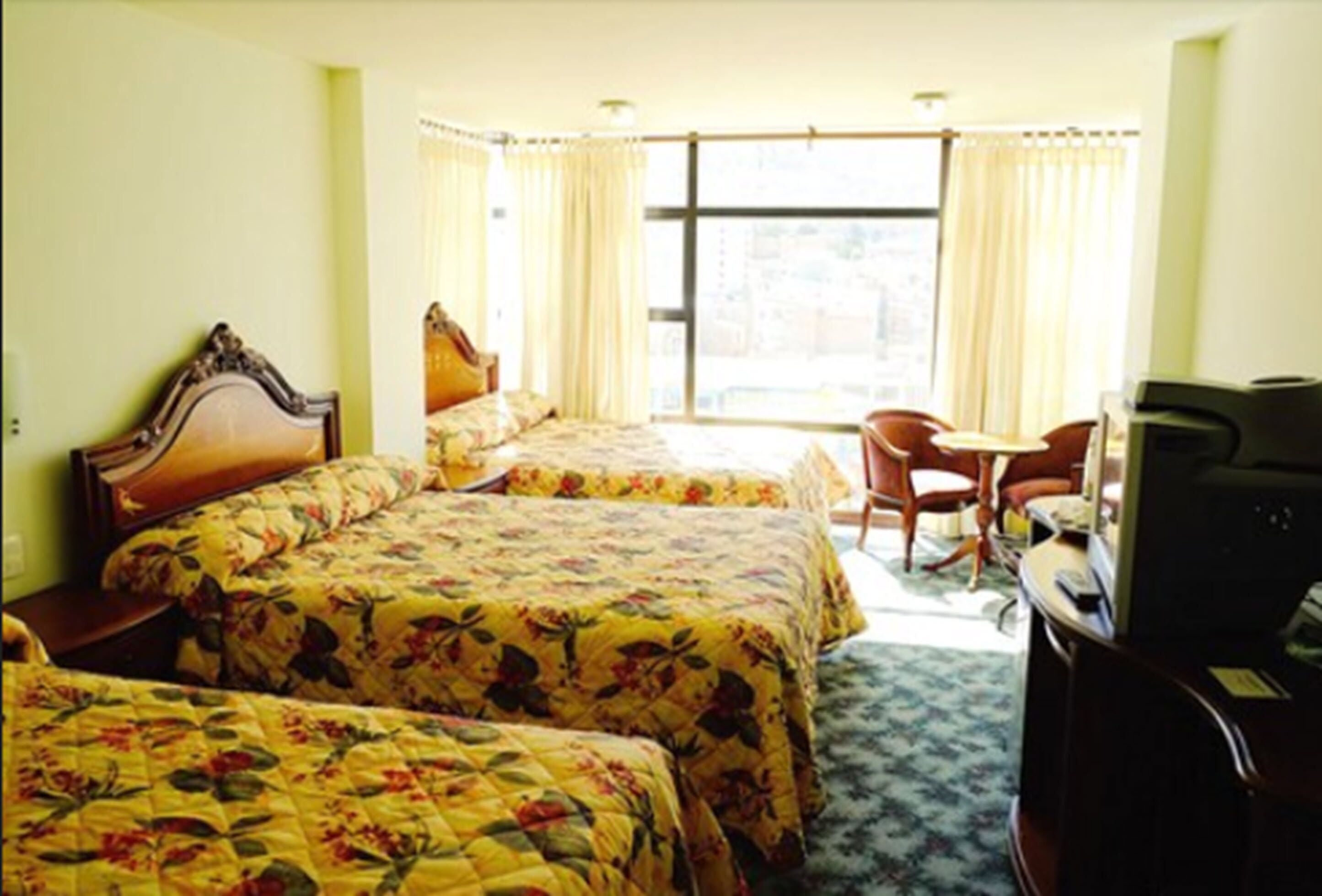 A hotel room with two beds, a desk, a chair, and a television.