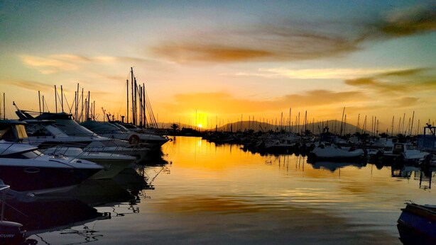 Un puerto deportivo con barcos amarrados en aguas tranquilas que reflejan la puesta de sol.