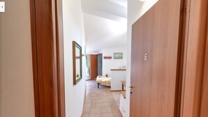 Un estrecho pasillo con puertas de madera y suelo de baldosas, que conduce a una habitación con una cama y una pequeña mesa.