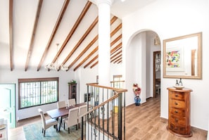 A spacious dining area with a wooden table and chairs, a staircase with wooden railings, and a large mirror on the wall.