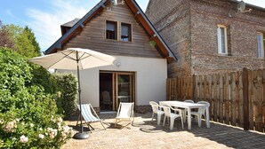 Een houten huis met een aanbouw van baksteen, een terras met tafel en stoelen, en een grote parasol.