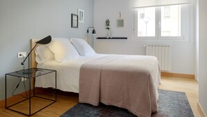 Ett sovrum med en säng, ett sängbord med en lampa, ett element och ett fönster med persienner.