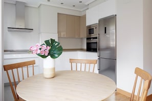 A modern kitchen with white cabinets, a stainless steel refrigerator, and a round wooden table with chairs.