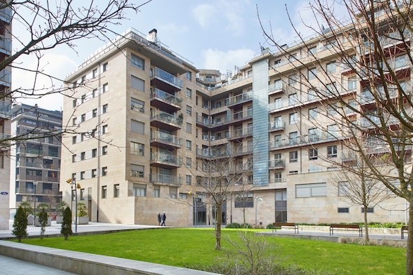 A multi-story residential building with balconies, a central courtyard, and a grassy area.
