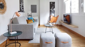 Ett modernt vardagsrum med en grå soffa, två pallar, ett soffbord, en golvlampa, en tv och konstverk på väggarna.