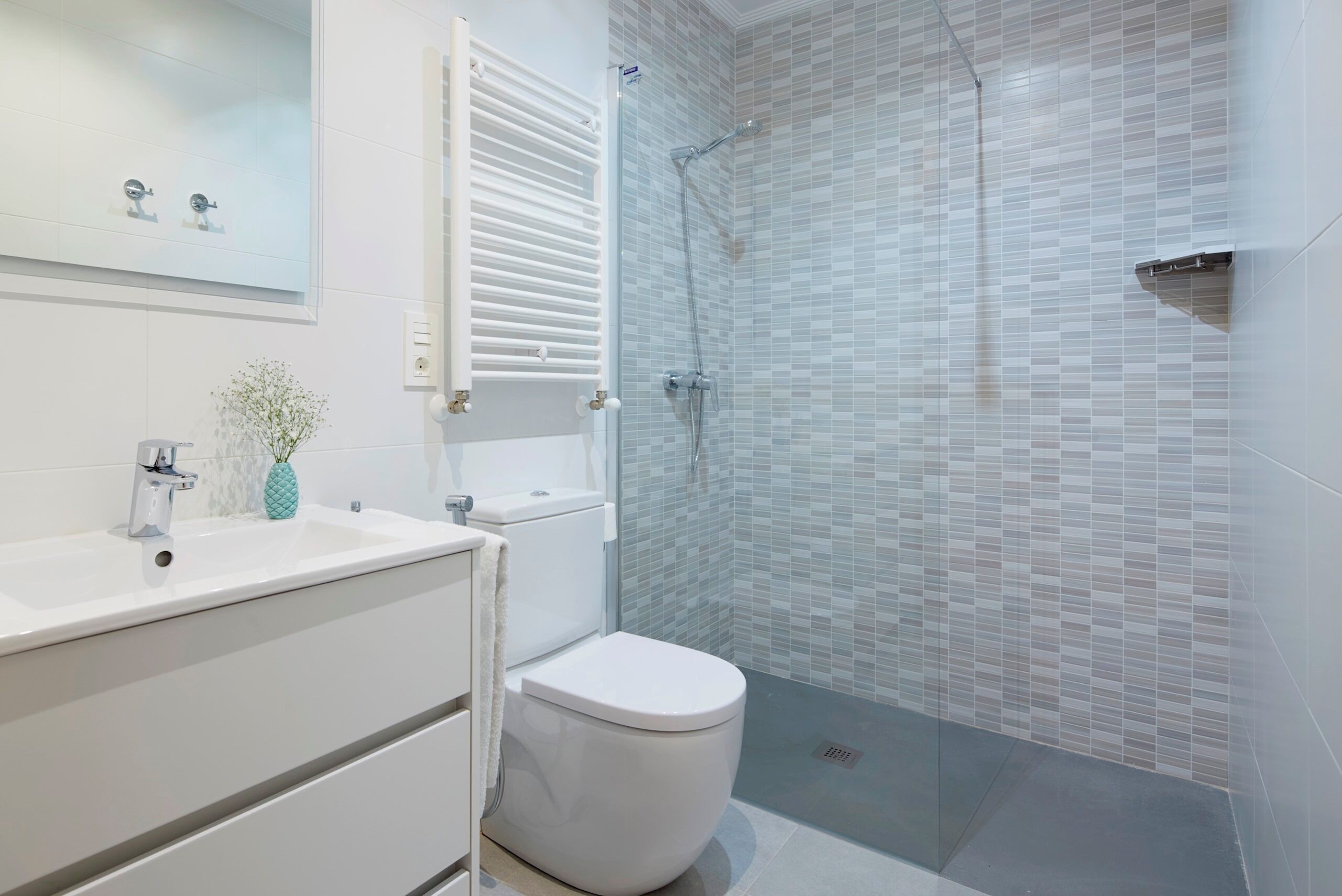 A modern bathroom with a white sink, toilet, and shower area with tiled walls.