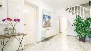 Un pasillo con piso de mármol, una escalera, una puerta, un cuadro y una planta en maceta.