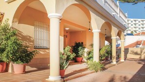 Un edificio con un patio cubierto, columnas, plantas en macetas y una ventana con rejas.