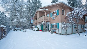 A two-story wooden house with a balcony, surrounded by snow-covered trees. - Alpine Villagers (Leavenworth)