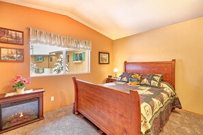 A bedroom with a wooden bed, a nightstand, a fish tank, and a window with a view of a house. - Alpine Villagers (Leavenworth)