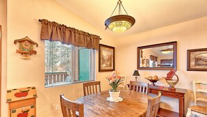 A dining room with a wooden table, chairs, a chandelier, a window with shutters, and a clock on the wall. - Alpine Villagers (Leavenworth)