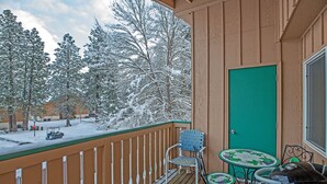 A wooden deck with a green door, a small table with chairs, and snow-covered trees in the background. - Alpine Villagers (Leavenworth)