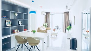 Una sala de estar moderna con un sofá blanco, una mesa de comedor con sillas, una estantería y una planta en maceta.