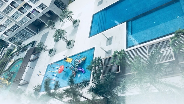 Un edificio moderno con una amplia piscina azul, varios balcones y abundante vegetación.