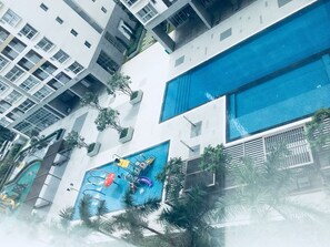 A modern building with a large blue swimming pool, multiple balconies, and lush greenery. - La Rose Great view 14th 2 Br. Apartment (Ho Chi Minh City)