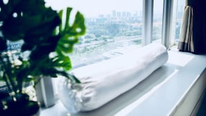 Una ventana con vista a la ciudad, un almohadón blanco en el alféizar y una planta en maceta.