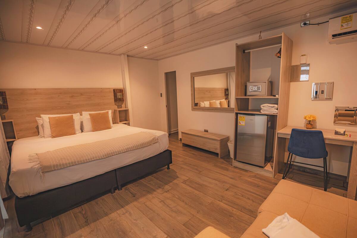 A hotel room with a bed, a desk, a chair, a mirror, and a bench.