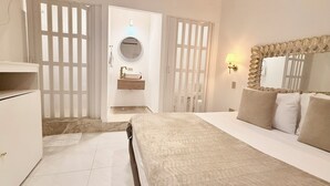 Quarto de hotel com cama, mesa de cabeceira, espelho, lavatório fixado na parede e janela com vista.