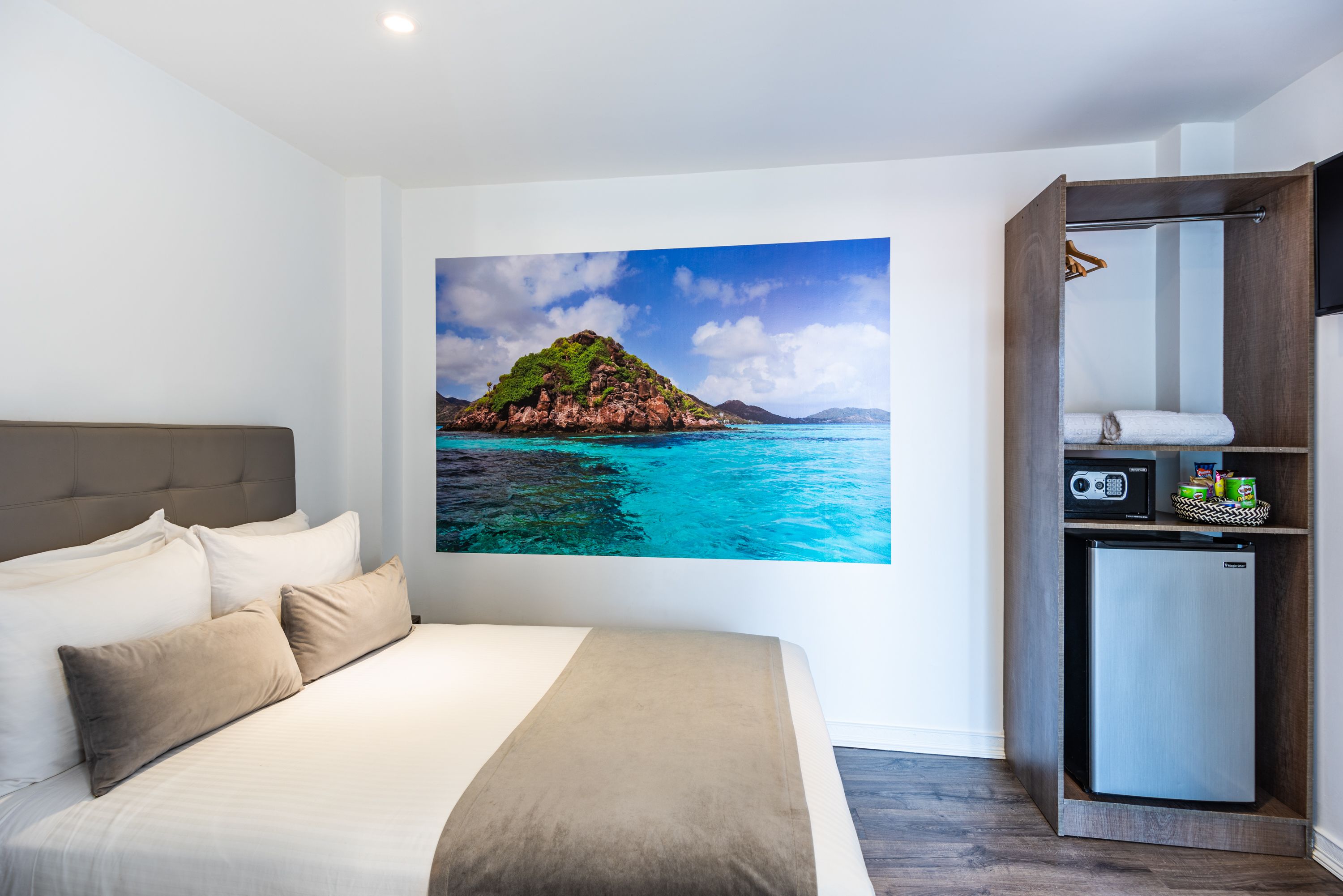 A hotel room with a bed, a wall-mounted TV, a small refrigerator, and a wooden wardrobe.
