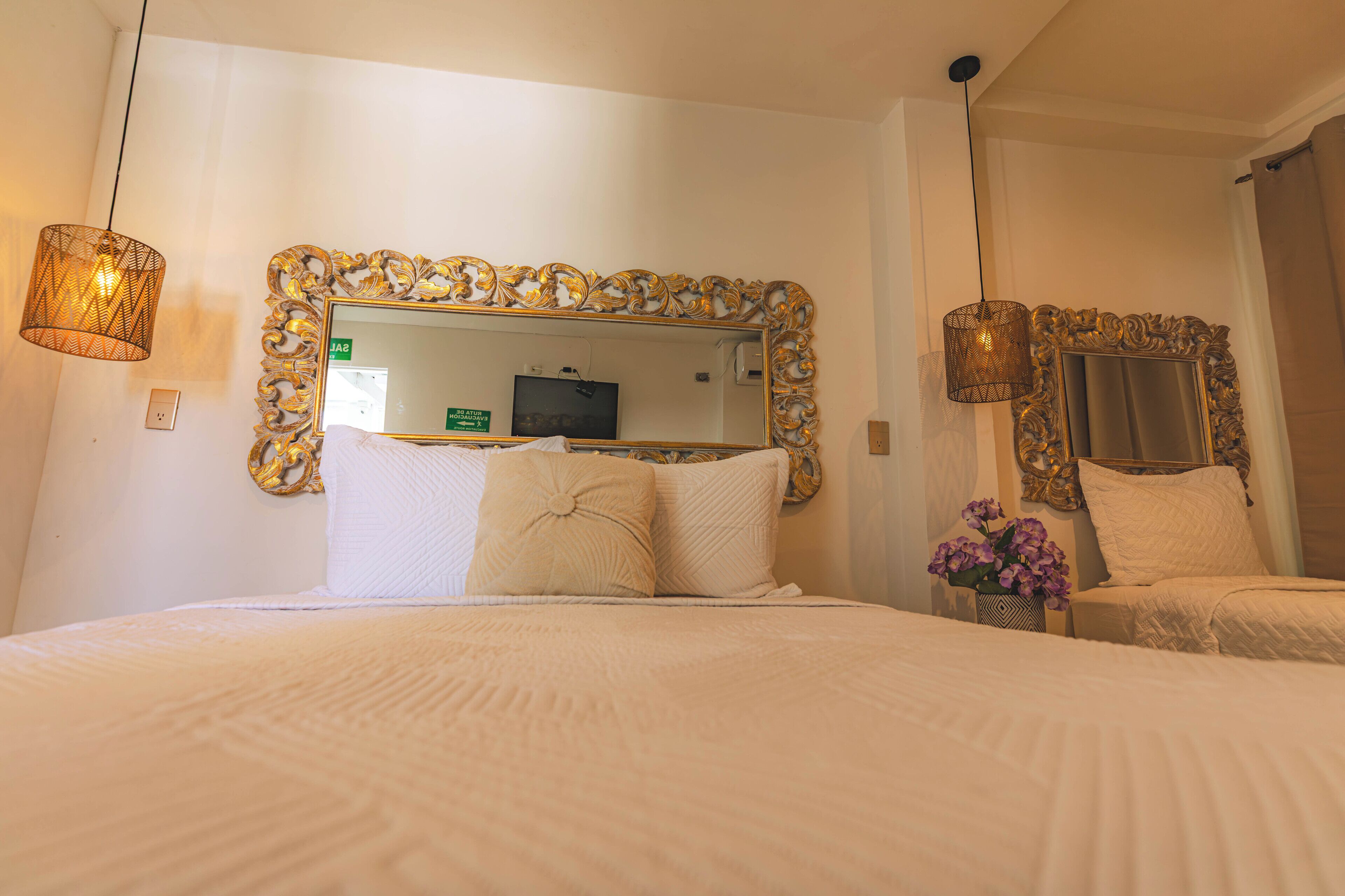 A hotel room with a large bed, two bedside tables, a mirror with an ornate frame, and a hanging light fixture.