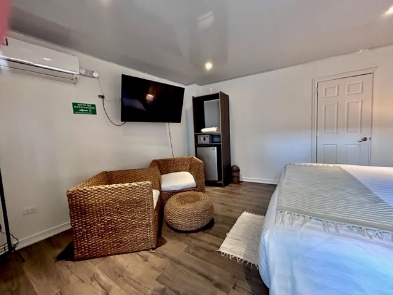 A hotel room with a bed, a television mounted on the wall, a wicker chair, and a small table.