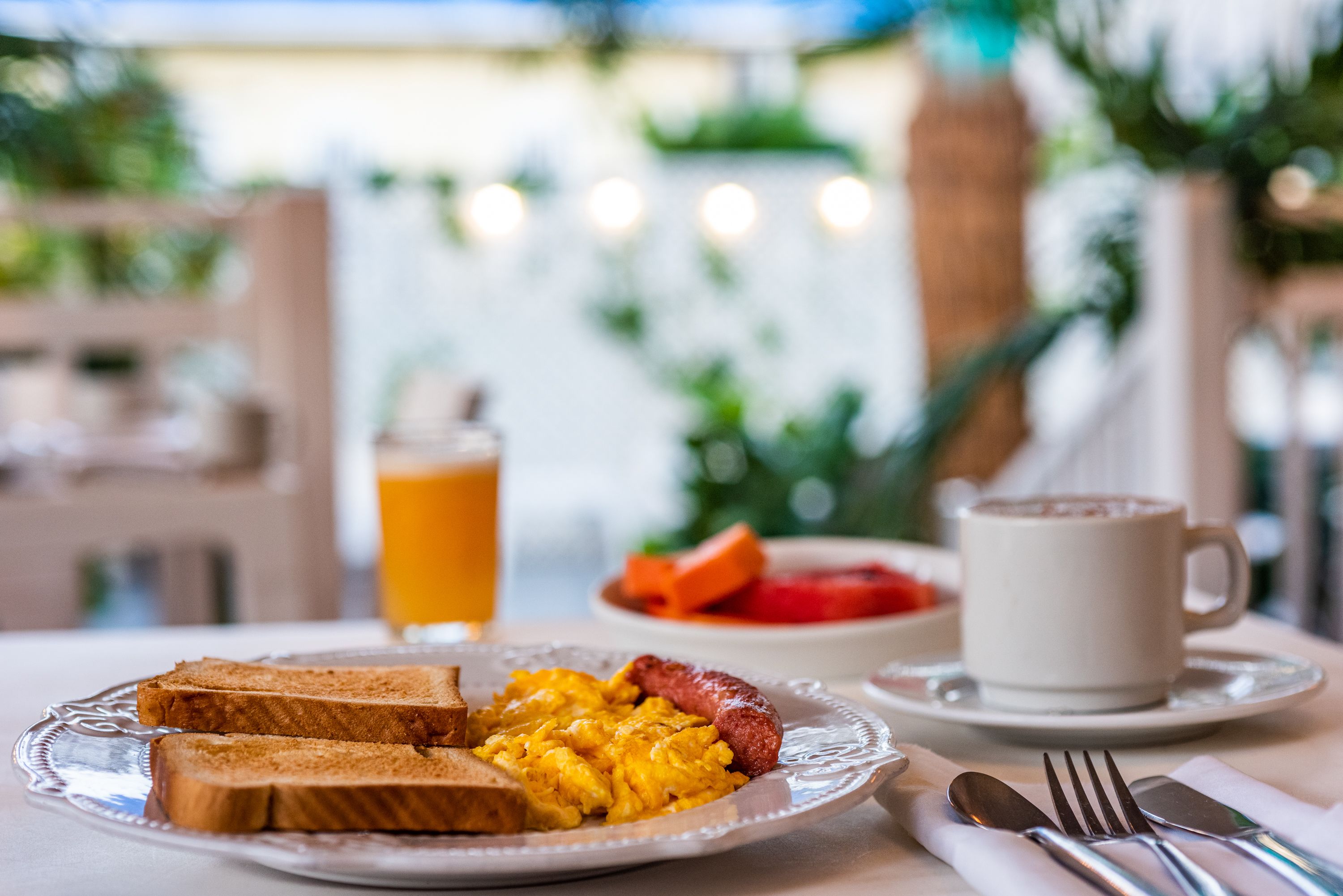 A breakfast setting with toast, scrambled eggs, sausage, a cup of coffee, and a glass of orange juice on a table.