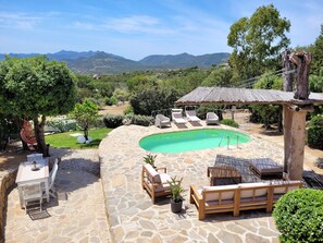 A poolside area with stone flooring, lounge chairs, a wooden table, and a hanging chair. - DELICIOUS HOUSE COMPLETELY RENOVATED (Punta Molara)