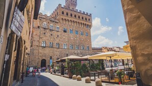 A historic building with a tower, outdoor seating area with umbrellas, and a paved walkway. - Il Gattopardo (Florence)