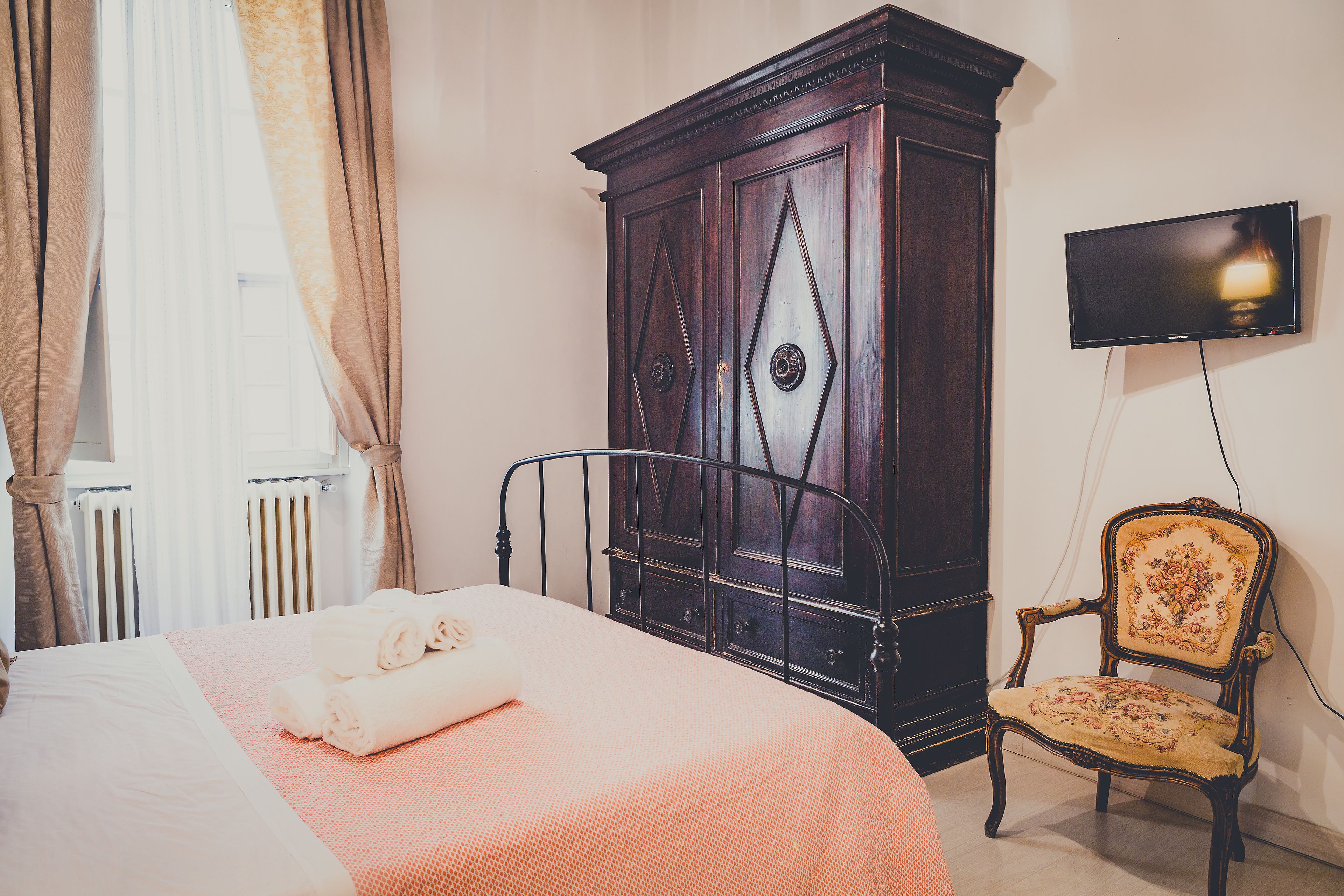 Una habitación de hotel con cama, armario, silla y televisión.